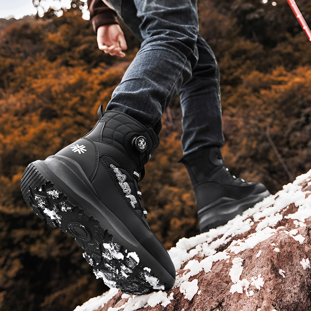 Black boot with its rubber tread showing, stepping onto a snowy rock