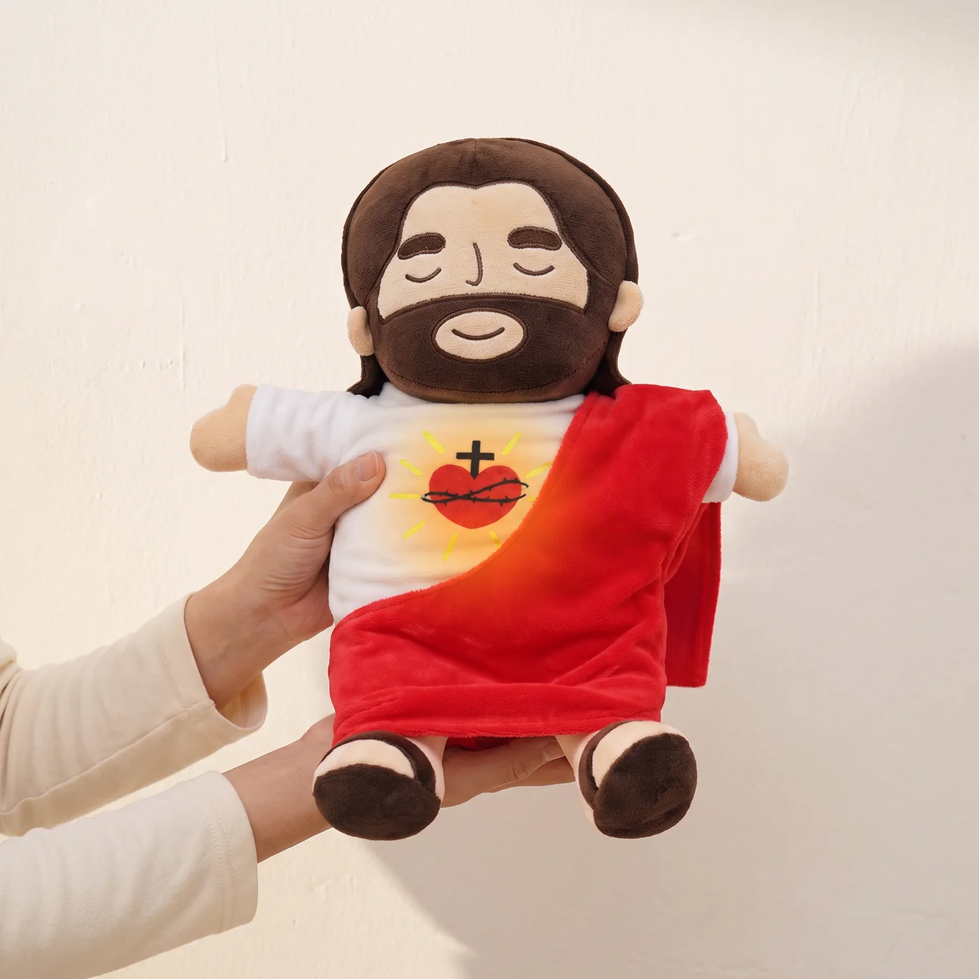 The plush held in two adult hands against a plain wall, showing its size