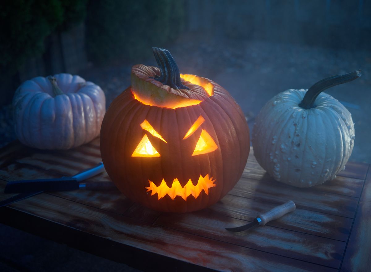 Close-up of a glowing jack o' lantern with eerie expressions on a wooden table under a misty night sky.
