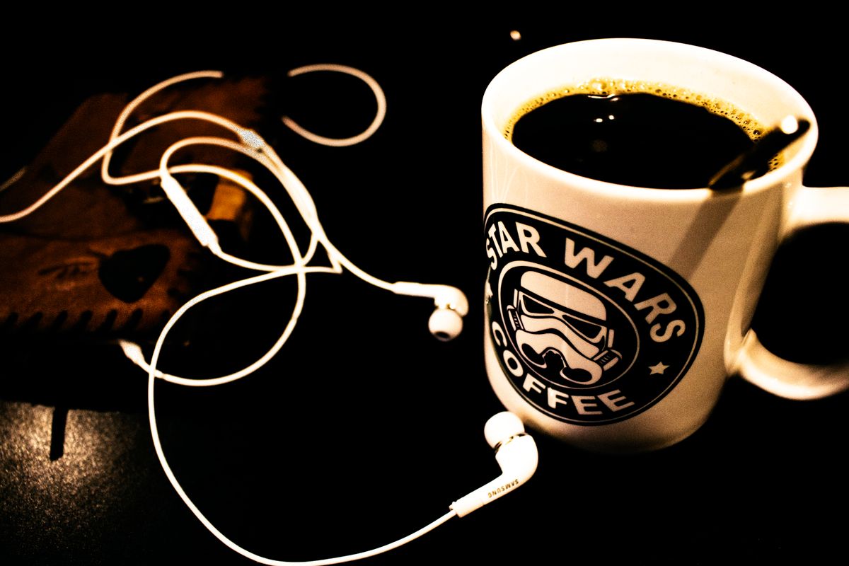 A dark-themed setup featuring a Star Wars coffee mug and headphones on a table.