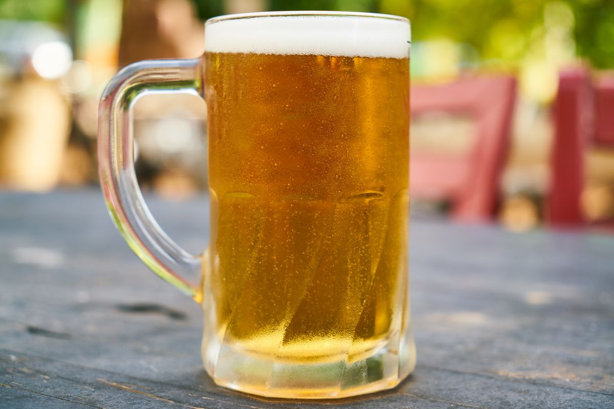 A refreshing cold beer in a clear glass mug set outdoors on a sunny day.