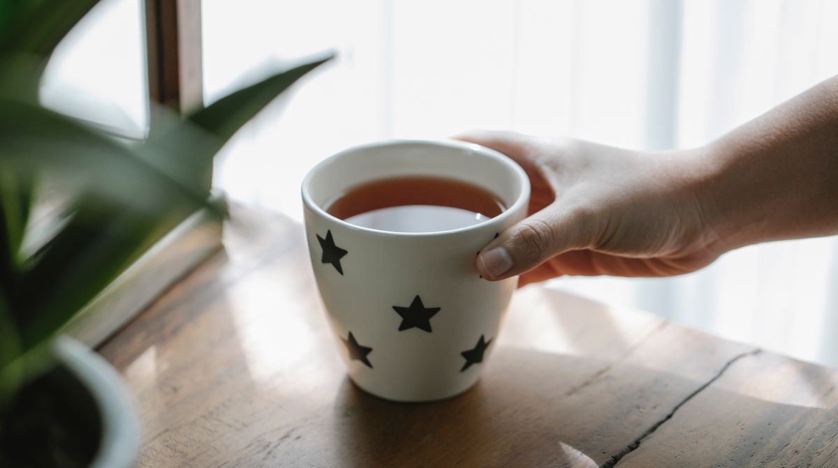 High angle of crop faceless person placing mug of hot aromatic delicious tea on wooden table