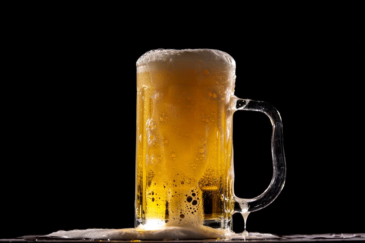Close-up of a full beer mug with frothy foam on top, beautifully contrasted against a black backdrop.