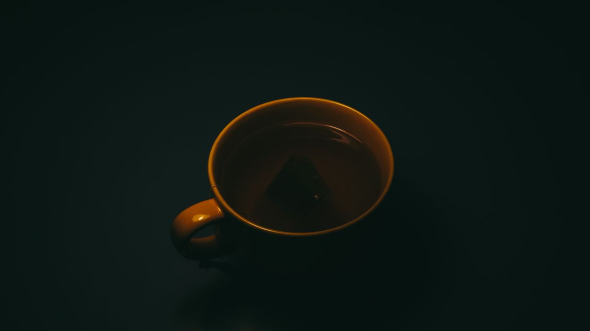 A close-up of a tea cup with an immersed tea bag against a dark background.