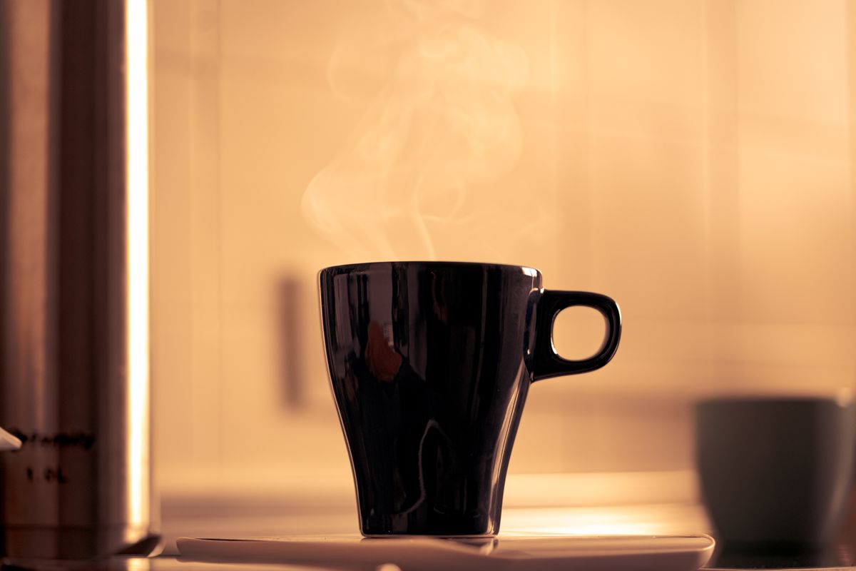A steaming black coffee cup on a saucer emits warmth in a cozy kitchen setting.
