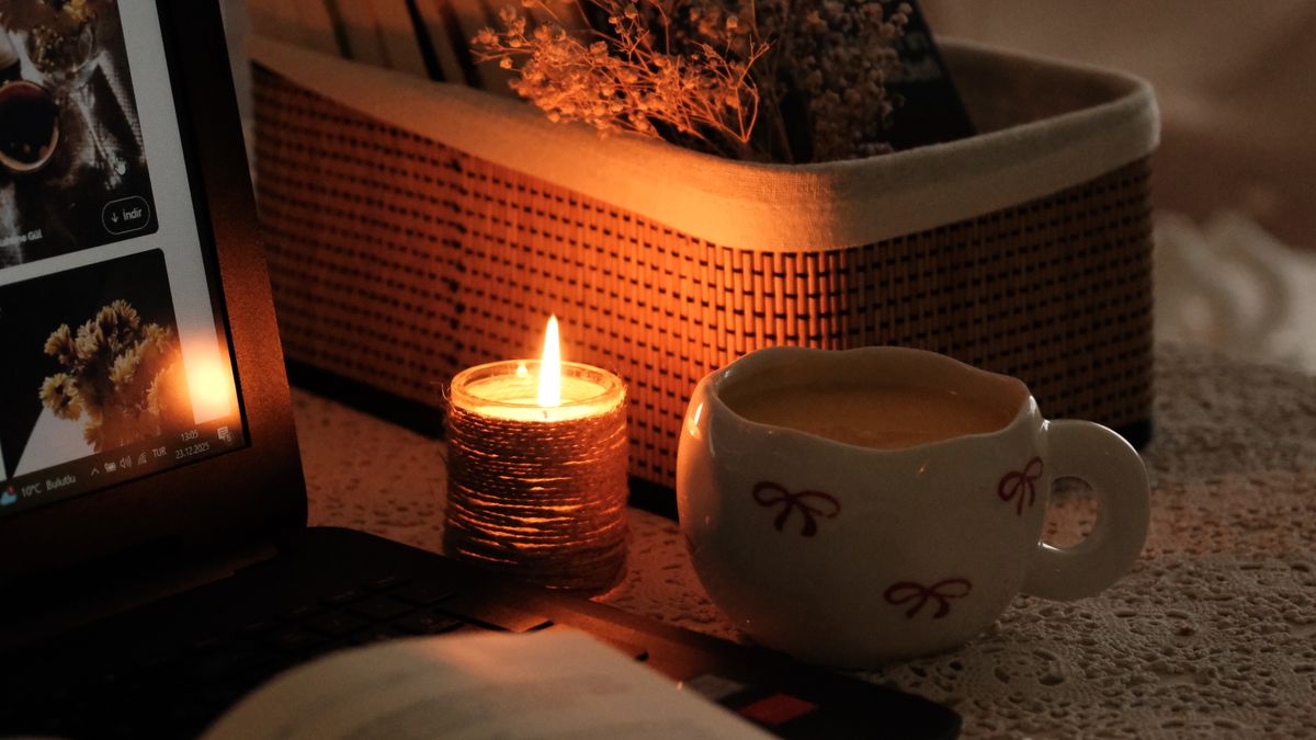A warm, ambient indoor scene featuring a lit candle and a cup of warm drink.