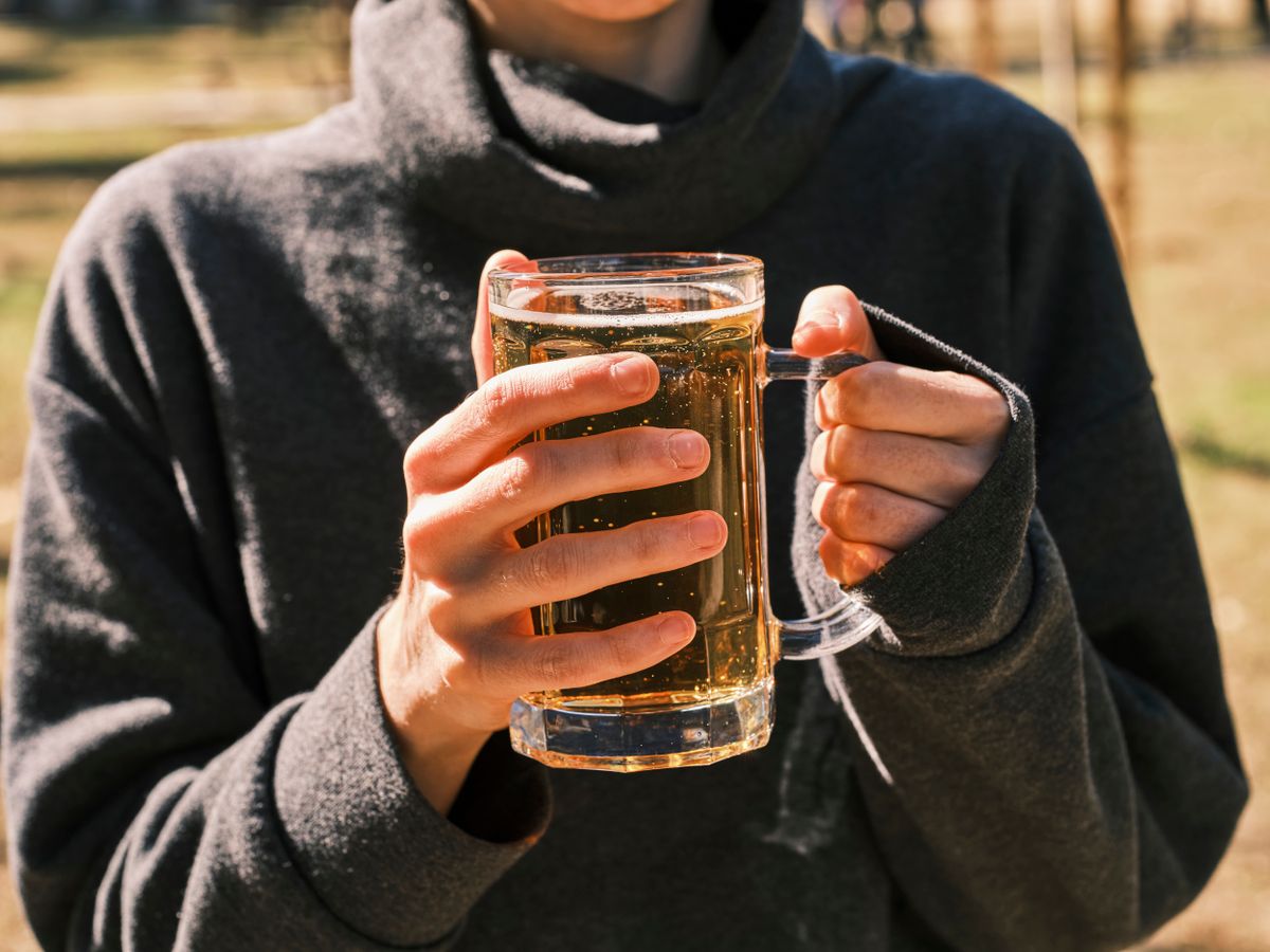 A person holding a mug of beer outside in a sunny setting, showcasing casual enjoyment.