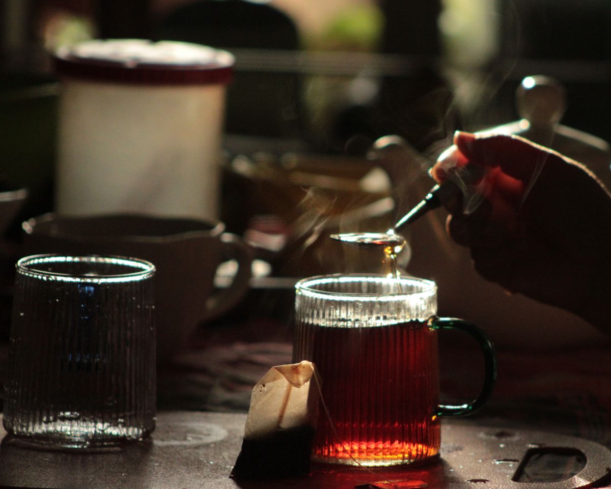 A hand pours tea into a glass mug in warm morning light, creating a cozy atmosphere.