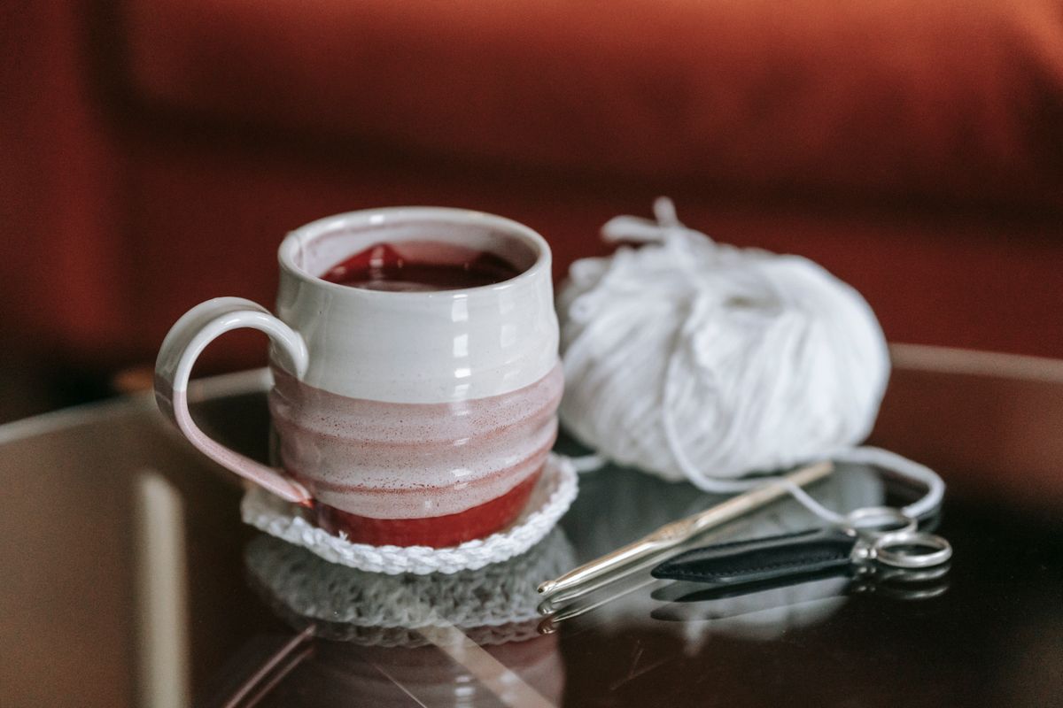 Close-up of a handcrafted mug with crochet and craft supplies on a table.