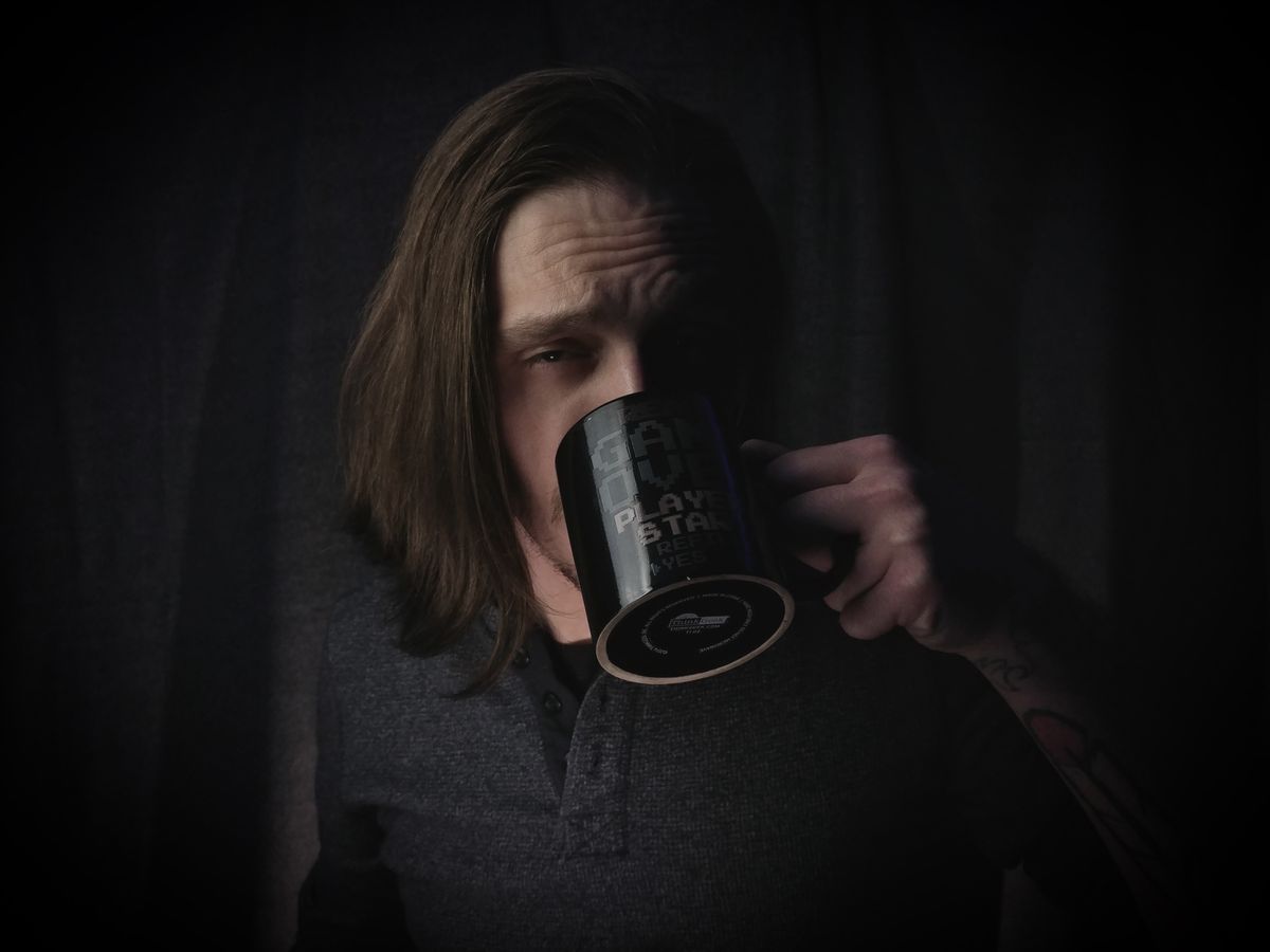 A moody portrait captures a man savoring a cup of coffee indoors.