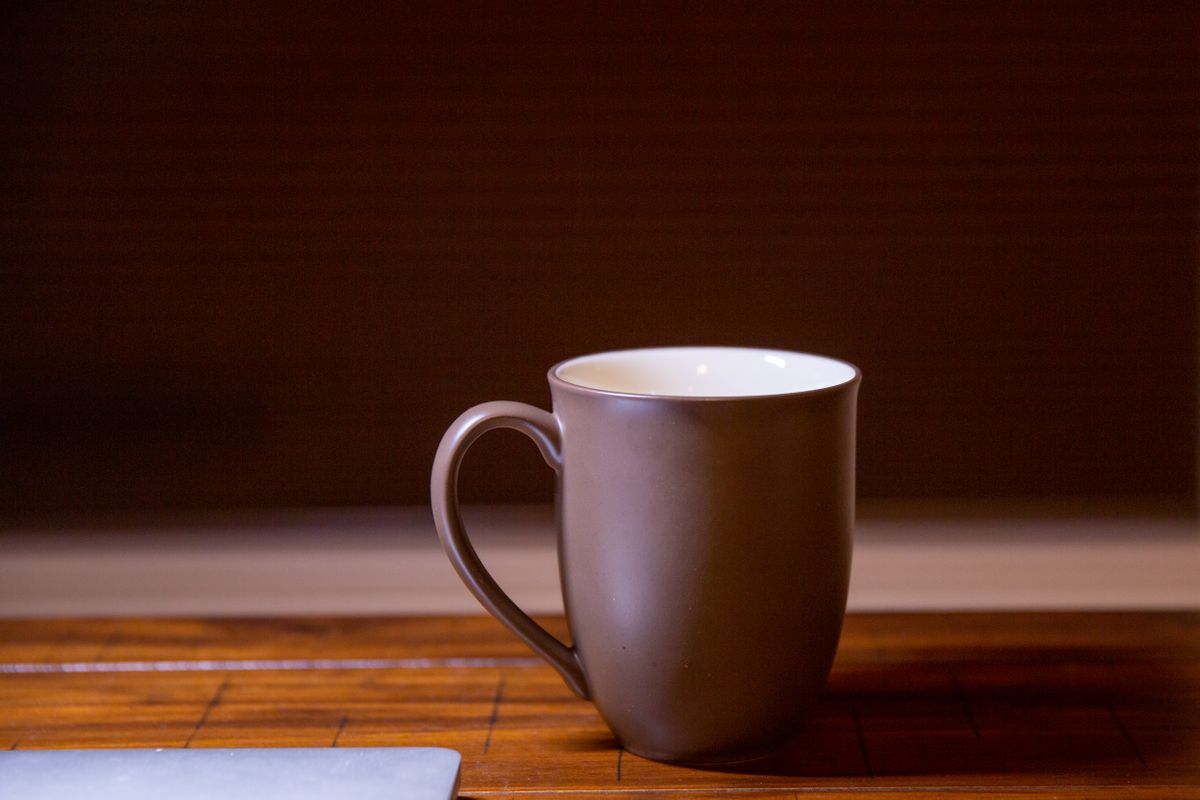 Simple brown ceramic mug on a wooden table with subdued lighting.