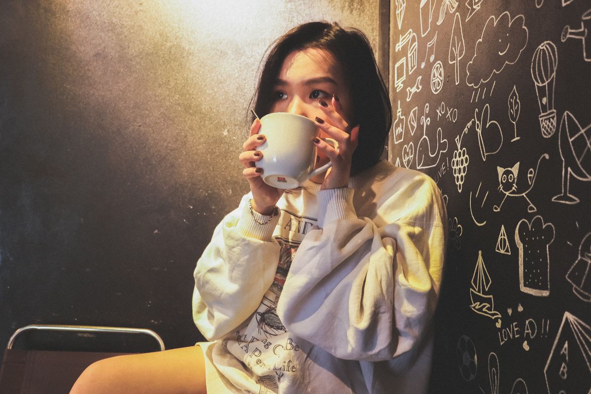 A young woman enjoying a cozy moment with a cup of coffee in a creatively designed studio space.