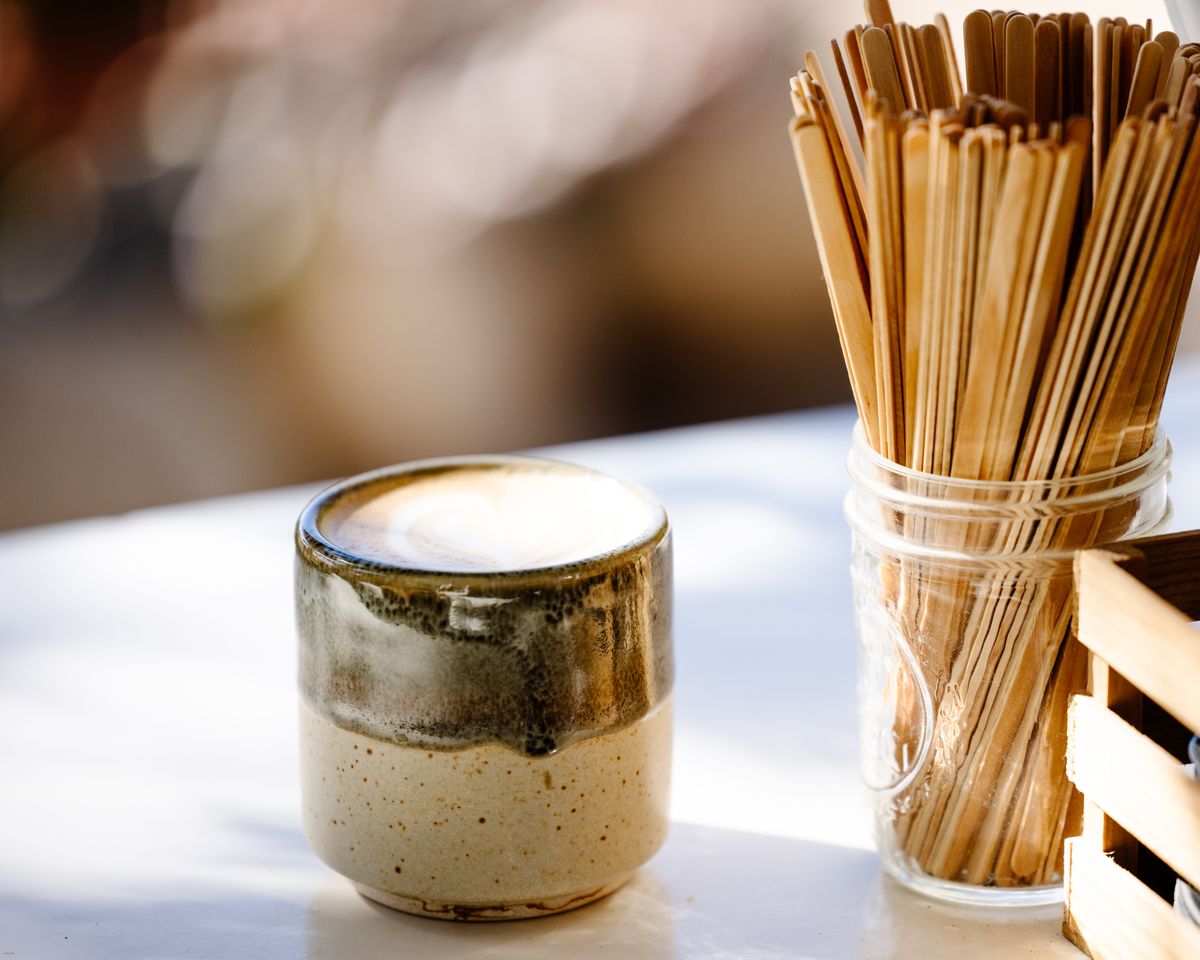A ceramic mug of coffee alongside wooden sticks on a sunlit table, creating a cozy atmosphere.