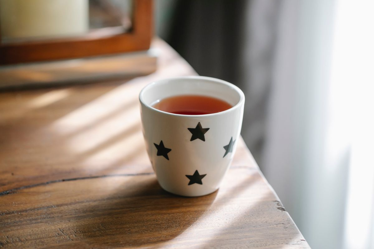High angle of white ceramic cup with stars of hot tasty tea placed on wooden table