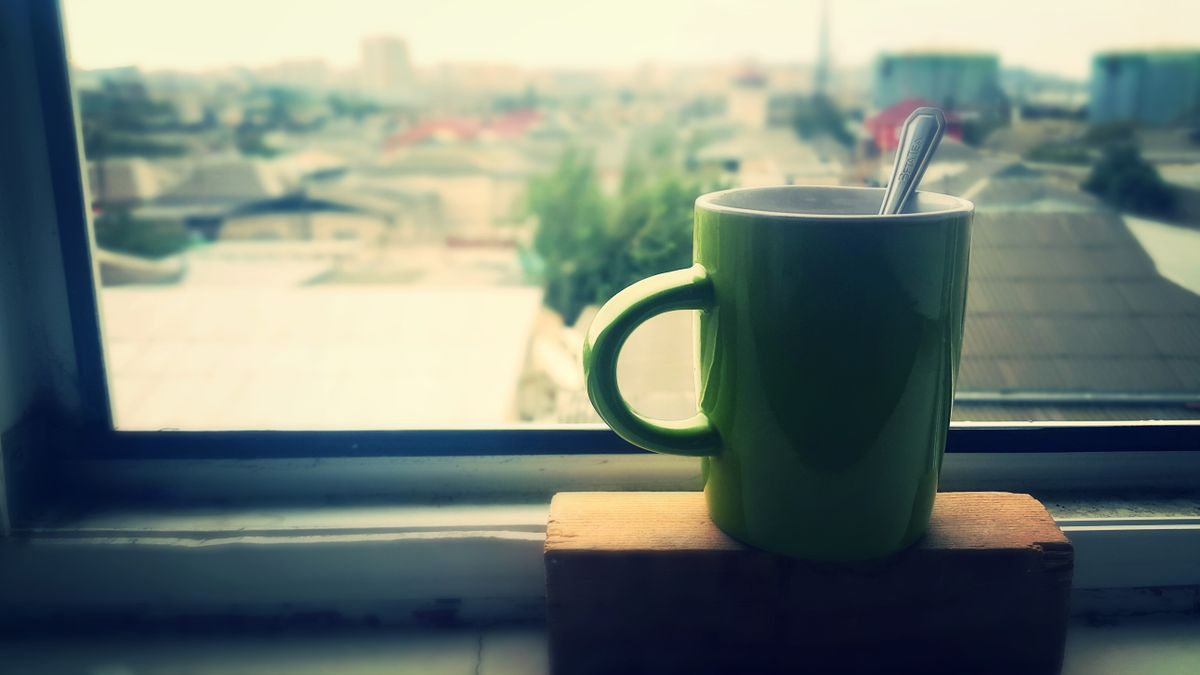 Green mug of coffee by window with urban view, creating a relaxing morning atmosphere.