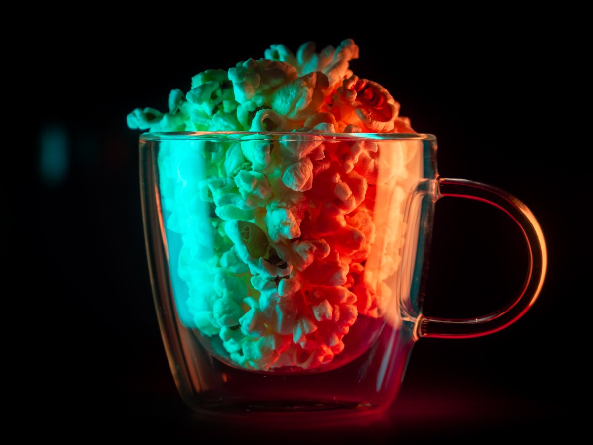 A vibrant and artistic capture of popcorn in a glass mug, enhanced with colorful neon lighting.