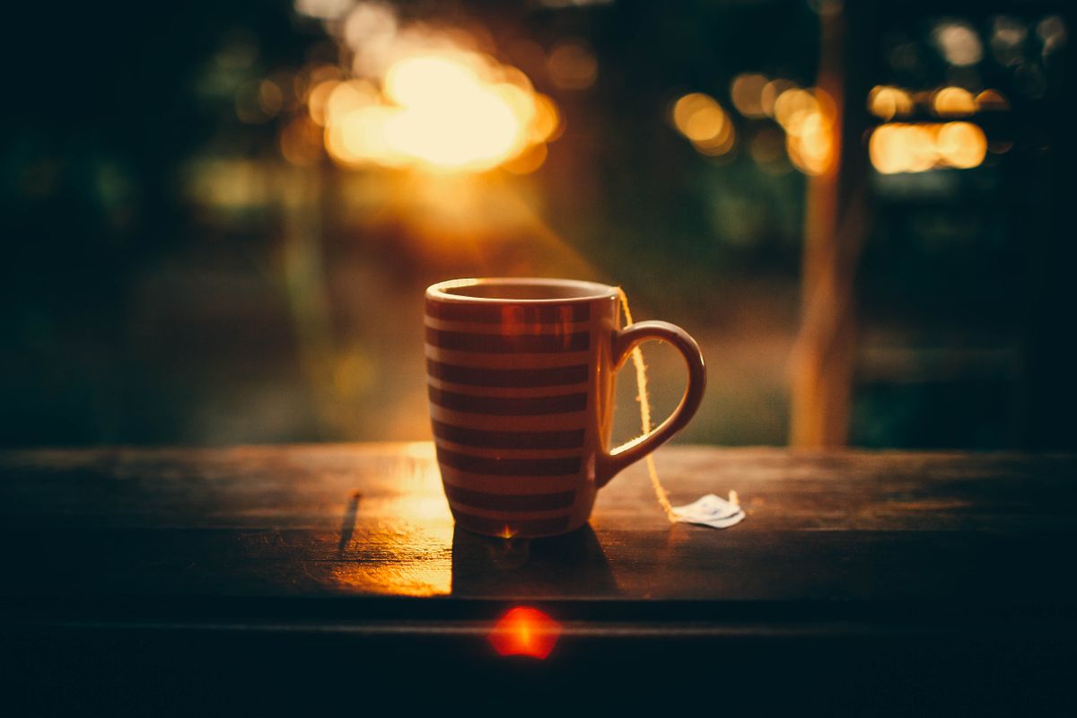 Ceramic mug of hot tea placed on wooden counter of cafe terrace under bright sun rays during sunset in tropical resort