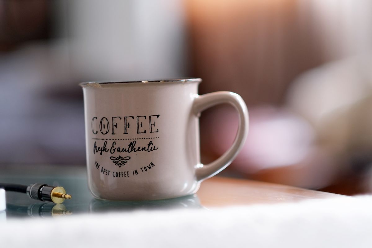 A ceramic coffee mug beside a headphone connector on a blurred indoor background.