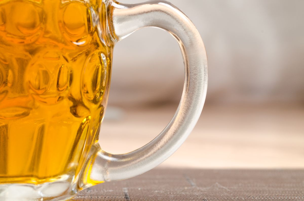 Detailed view of a frosty beer mug filled with golden ale on a wooden surface.
