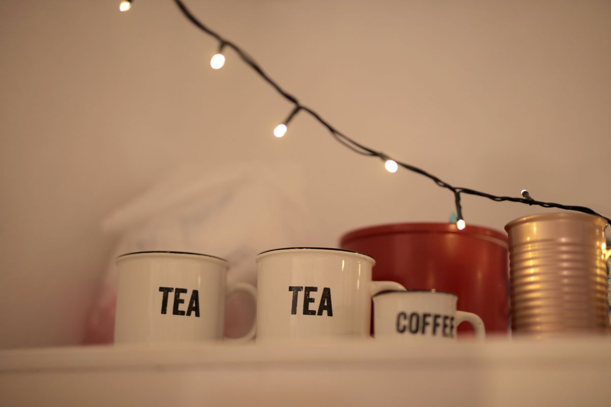 Warm indoor scene with mugs labeled 'Tea' and 'Coffee' under string lights.