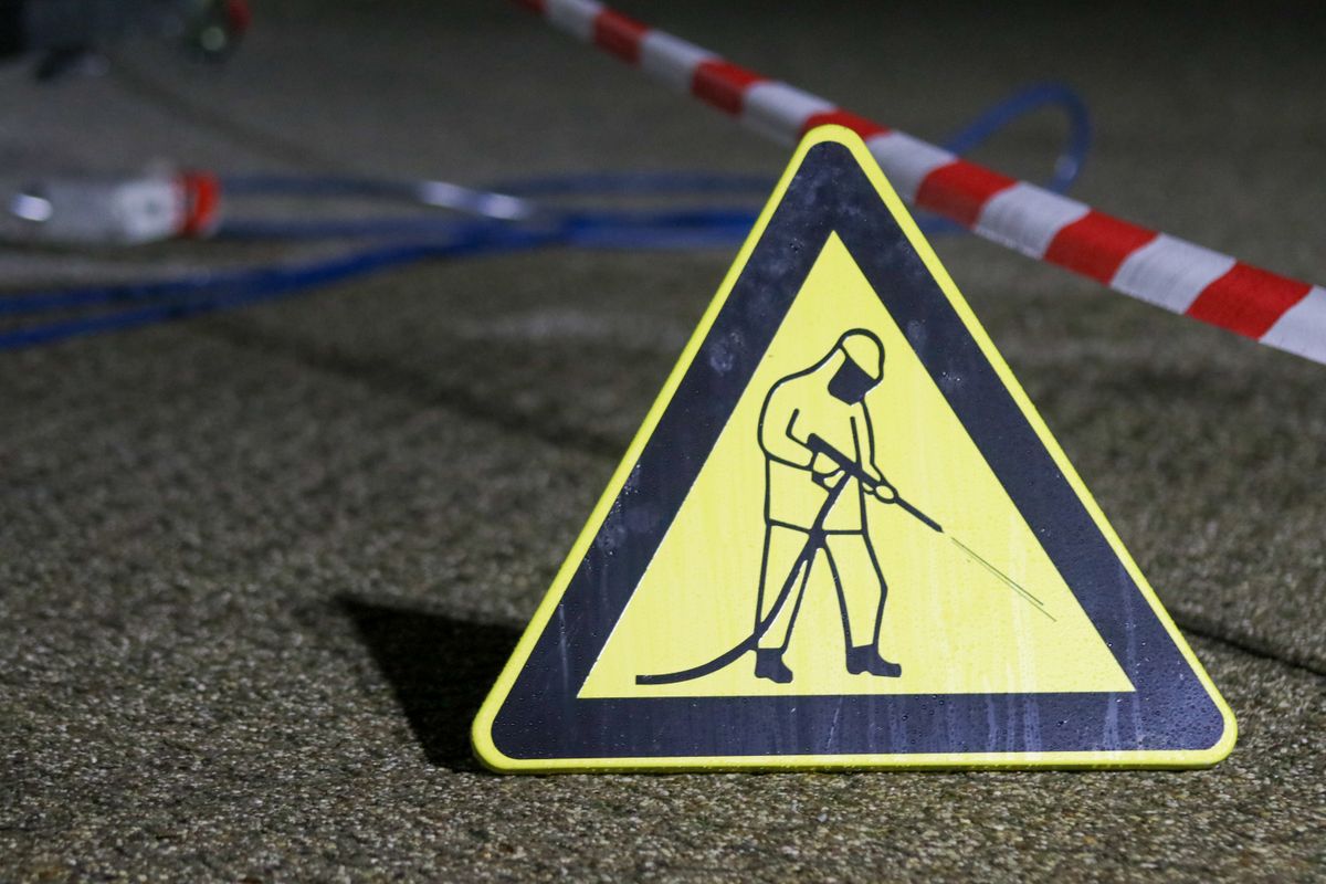 Yellow caution sign depicting pressure washing in a night setting with safety barriers.