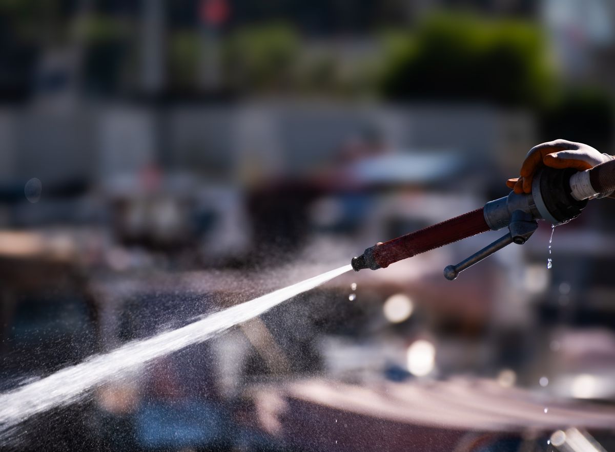 A close-up of a hand holding a water hose spraying in sunlight, Foça, Turkey.