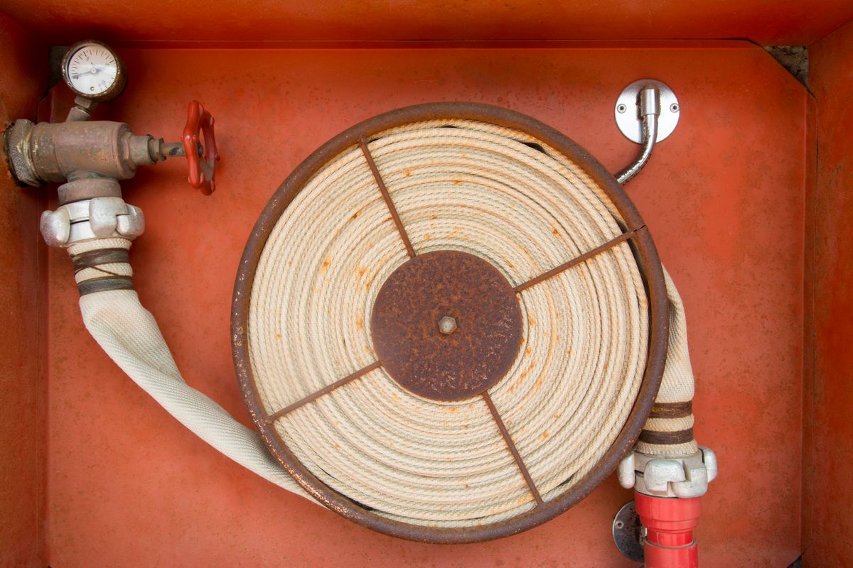Rusty rolled fire hose and valve in metal cabinet, safety equipment ready for emergency use.