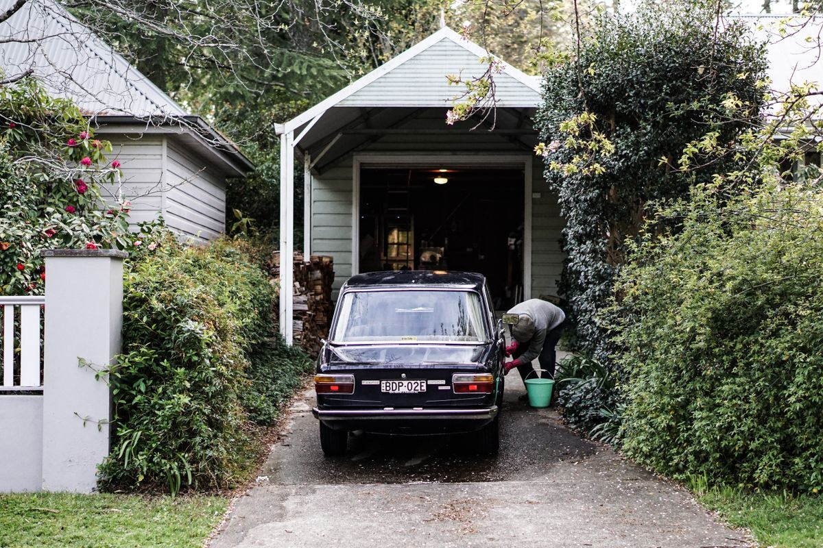 A classic automobile parked in a lush suburban driveway with a person cleaning it in Leura, NSW.