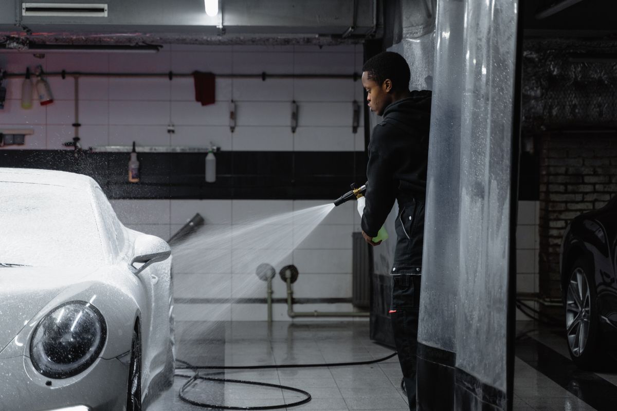 A person using a pressure washer to clean a car in an indoor garage setting.