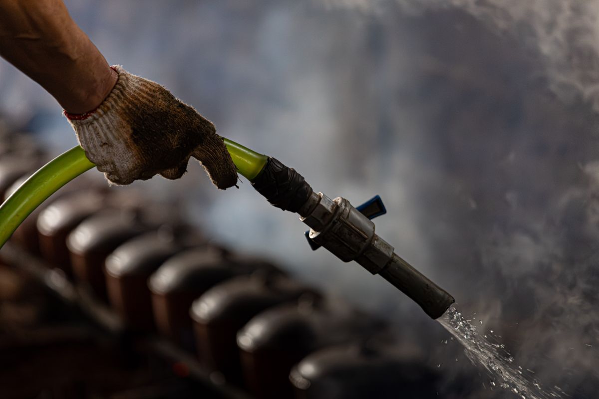 A gloved hand handling an industrial water hose with steam in the background.
