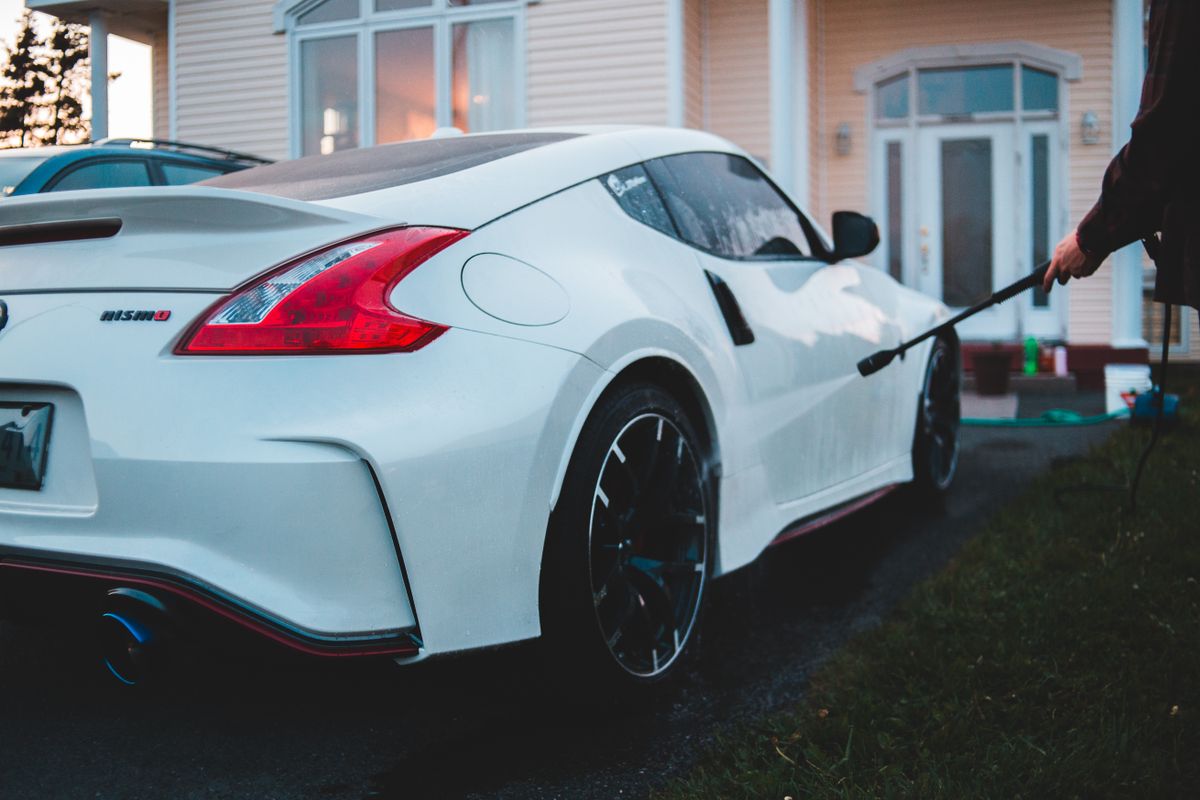 Close-up of a white Nissan 370Z sports car during a car wash with a hose.
