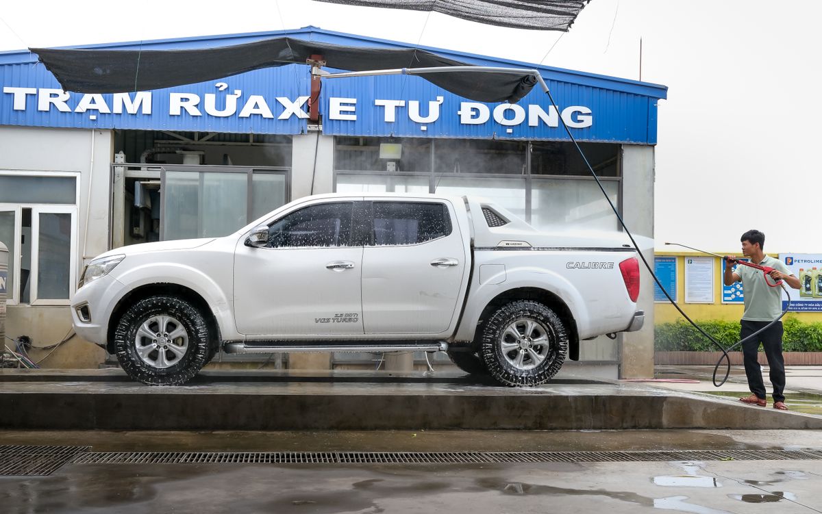 Adult using pressure washer to clean a white pickup truck at an outdoor car wash facility.