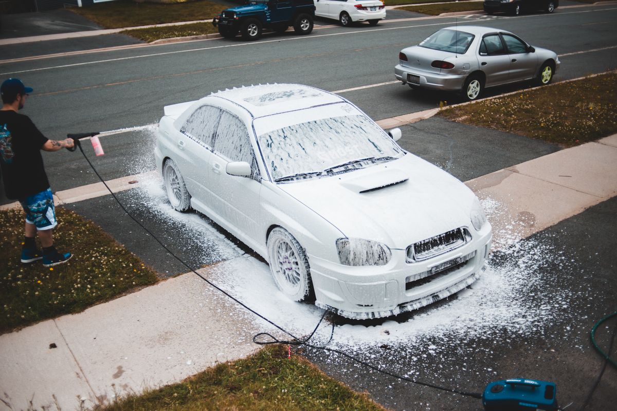 From above car covered in foam washing by man in casual wear with pressure washer gun in hand
