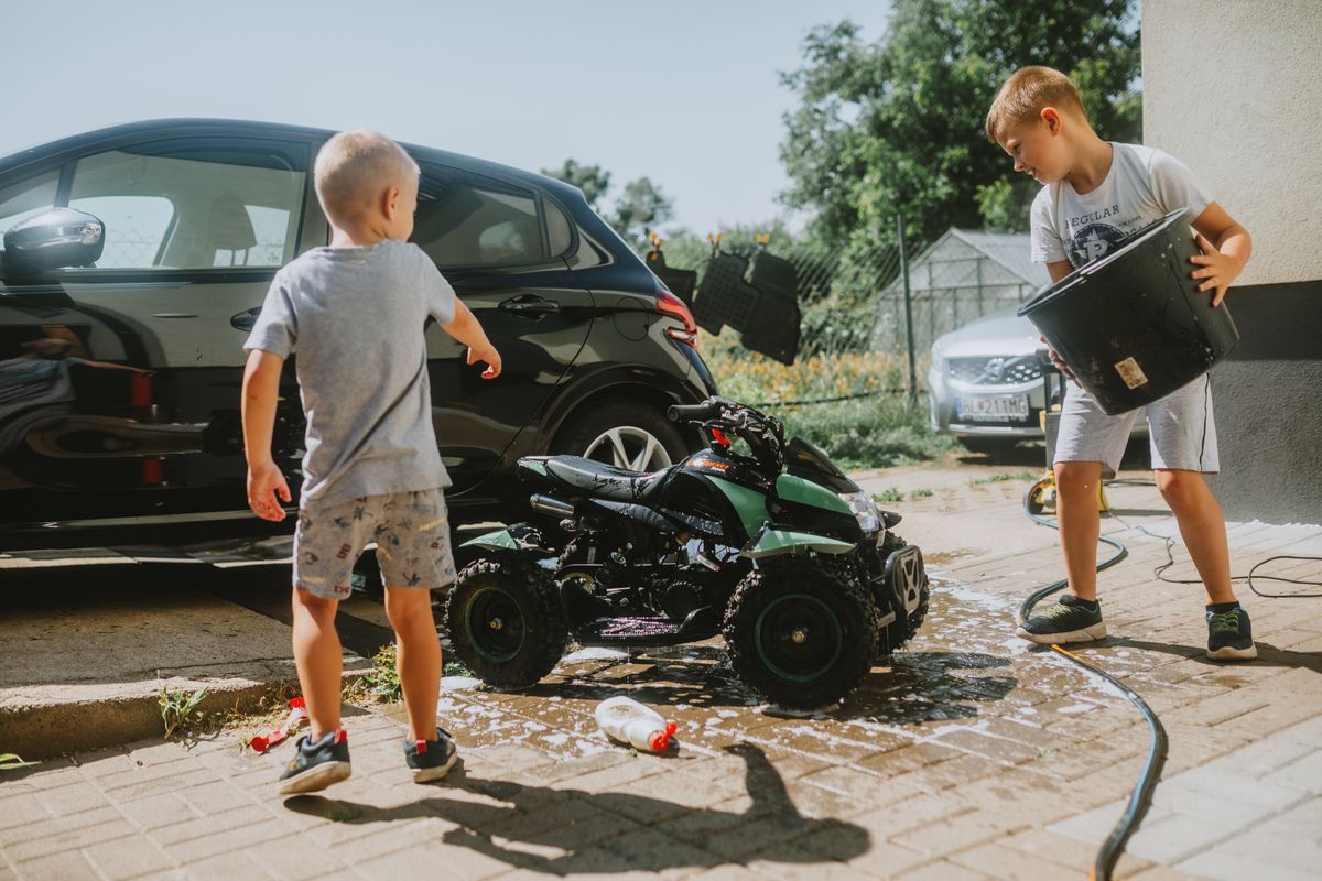 Two kids wash a toy car with soap and water on a sunny day. Fun and playful activity.