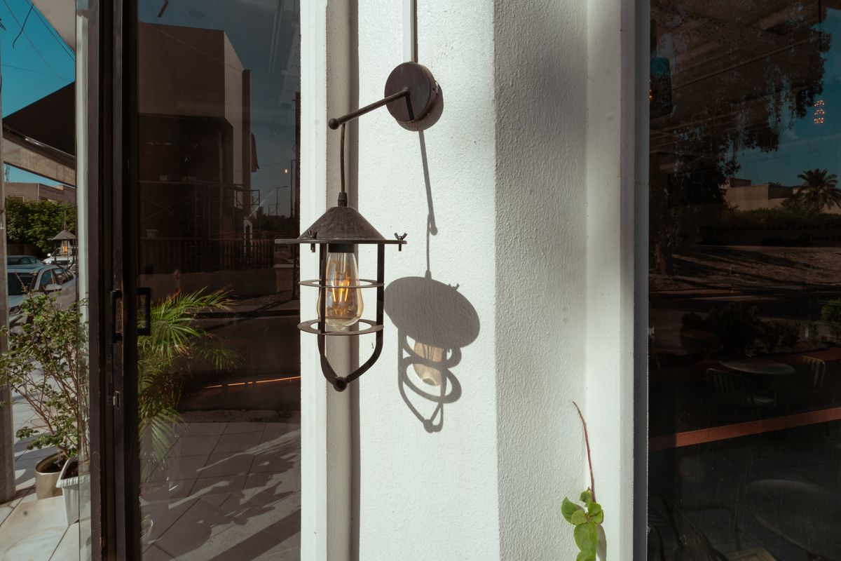 A vintage outdoor wall lantern casting a shadow on a sunny day in Baghdad, Iraq.
