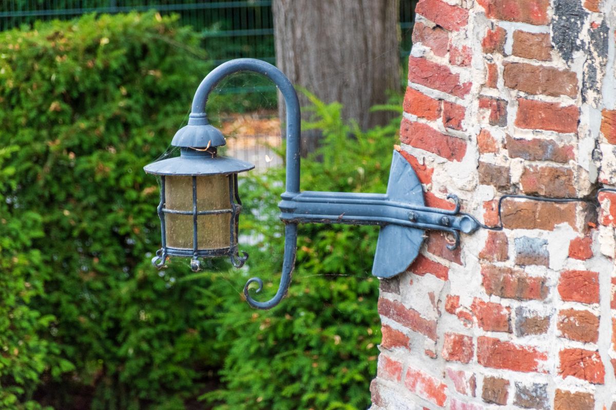 Charming vintage outdoor lantern mounted on rustic brick wall with green foliage background.