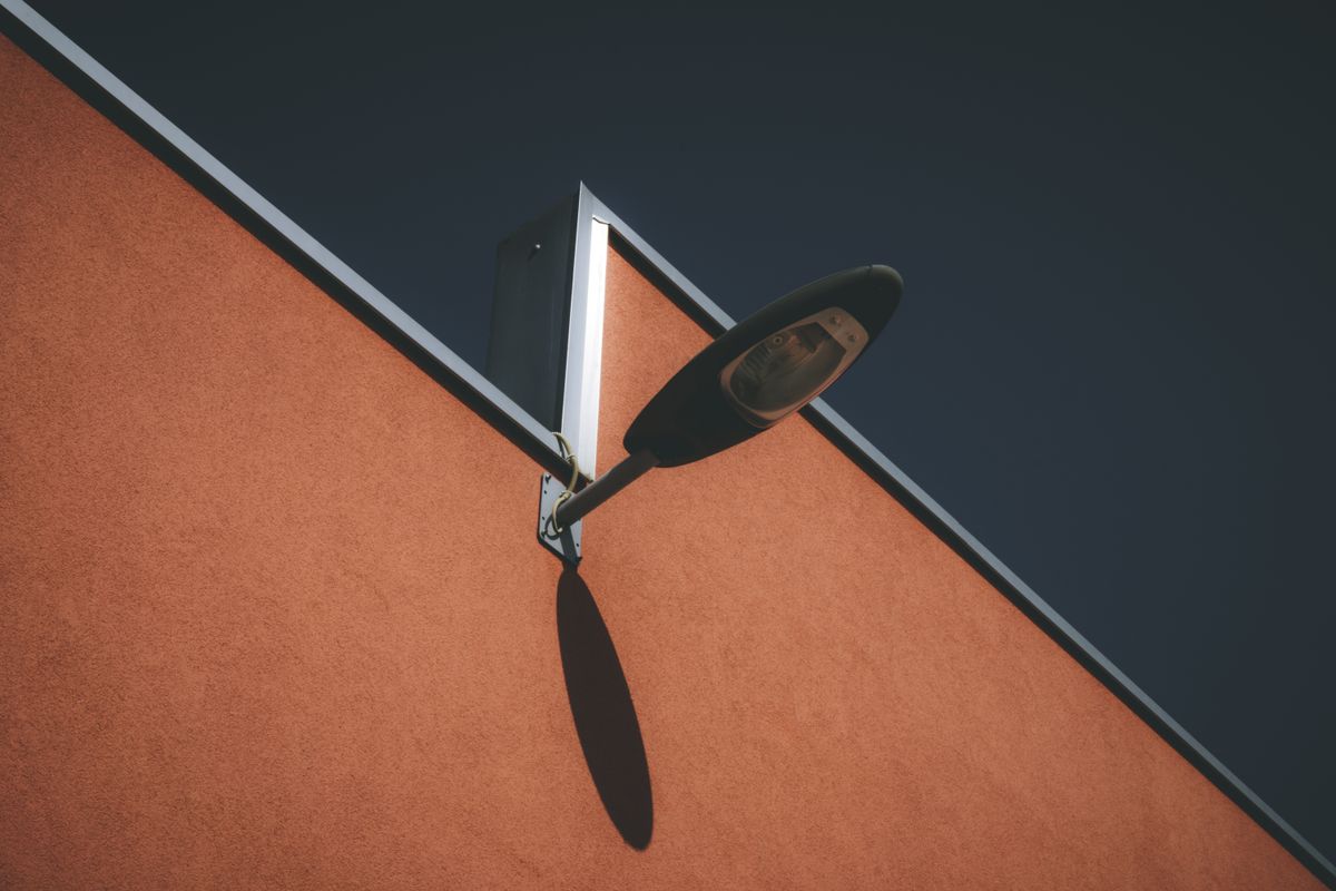 A minimalist outdoor wall lamp casting a distinct shadow against a modern building's façade.