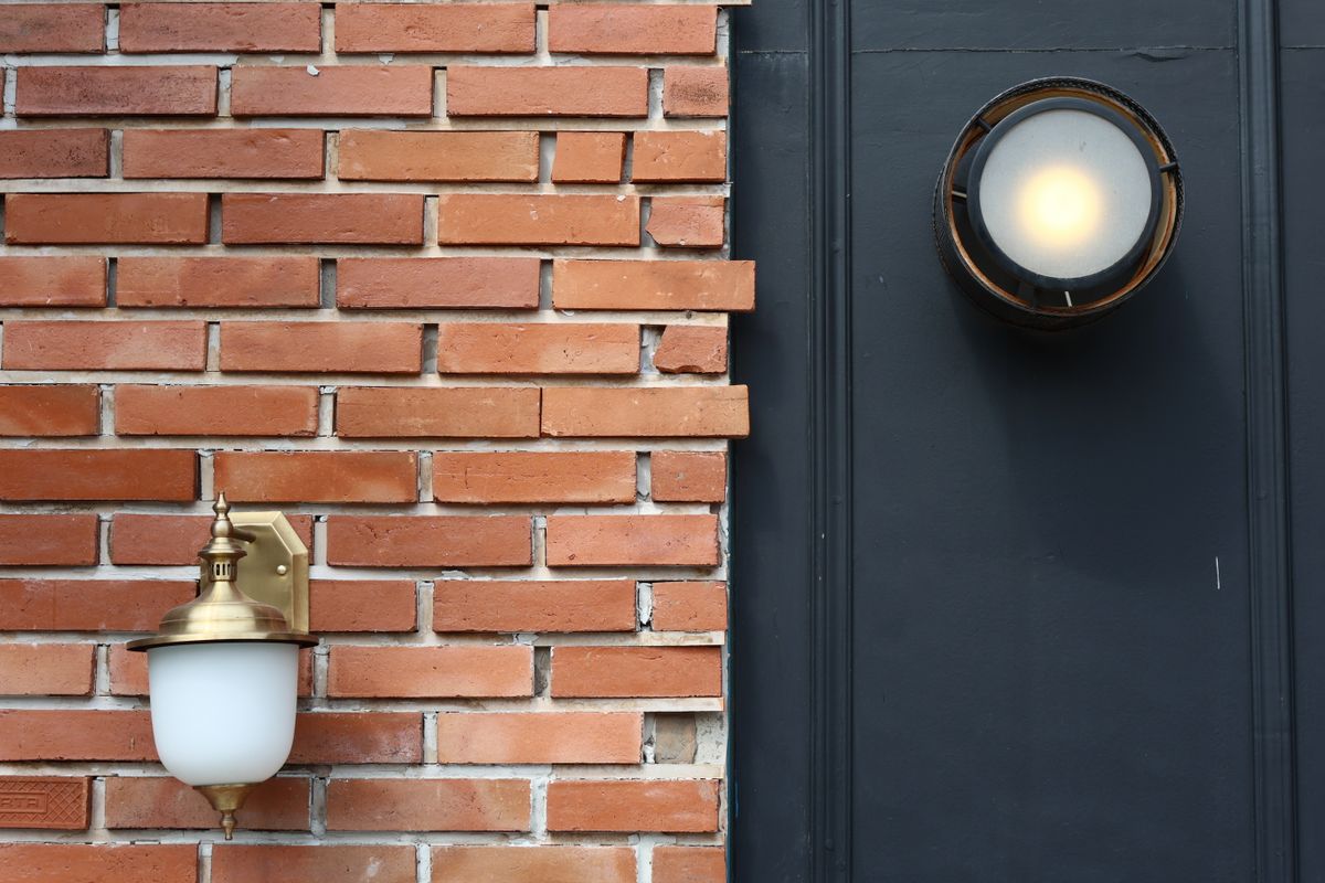 A rustic brick wall featuring two modern outdoor light fixtures, creating visual contrast.