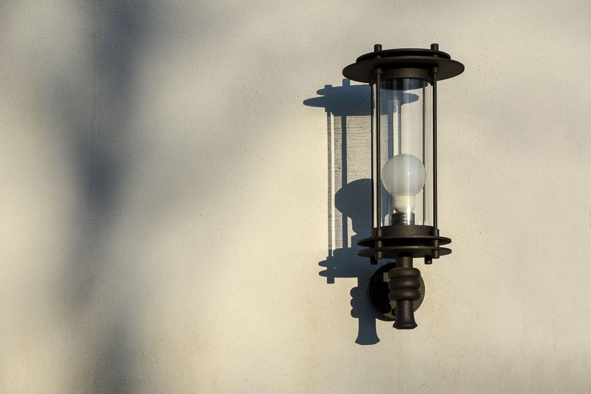Elegant outdoor wall light casting shadow on textured wall in sunlight.
