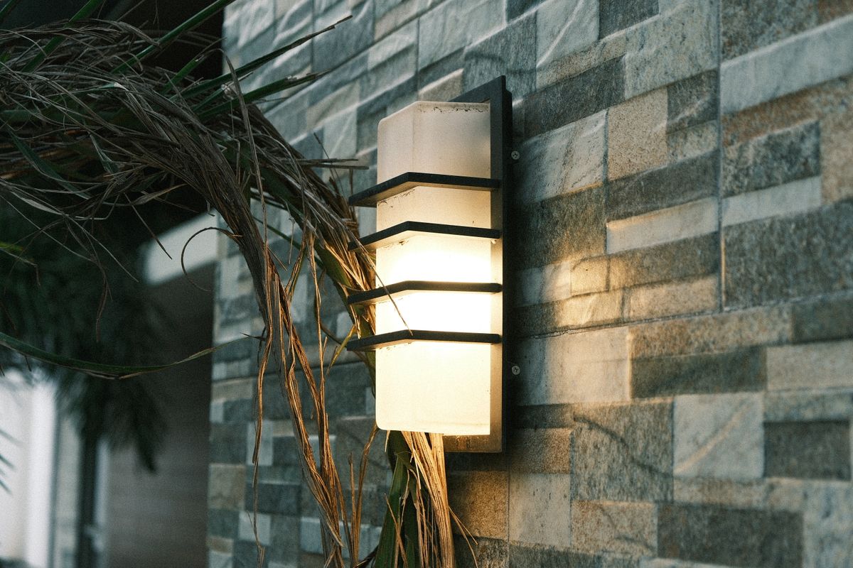 Illuminated outdoor wall lantern on a textured stone wall, surrounded by plants, setting a cozy evening ambiance.
