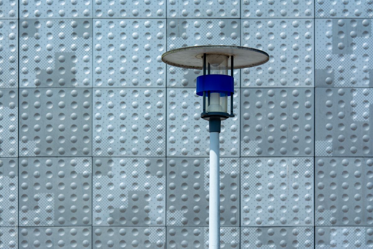 A modern solar lamp stands in front of a textured wall, showcasing urban design.