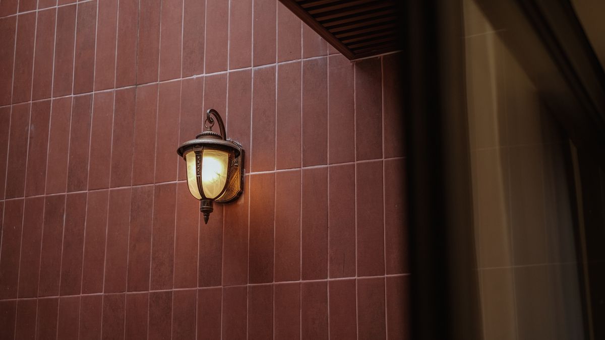 A vintage bronze wall lantern emits warm light against a red brick wall at night.