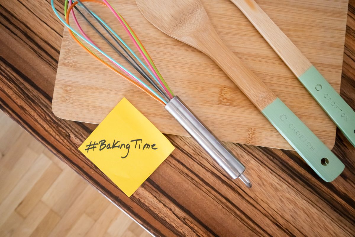 Top view of colorful kitchen utensils on a wooden board with a #BakingTime note.