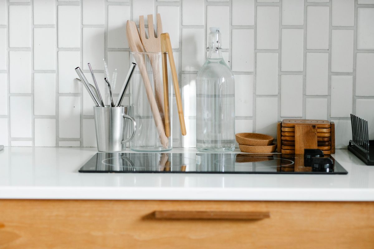 A modern minimalist kitchen counter featuring utensils, glass bottles, and a ceramic backsplash.