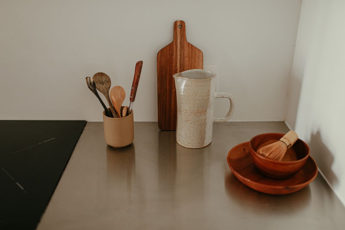 A serene kitchen setup featuring wooden utensils, a ceramic pitcher, and a whisk on a stylish countertop.