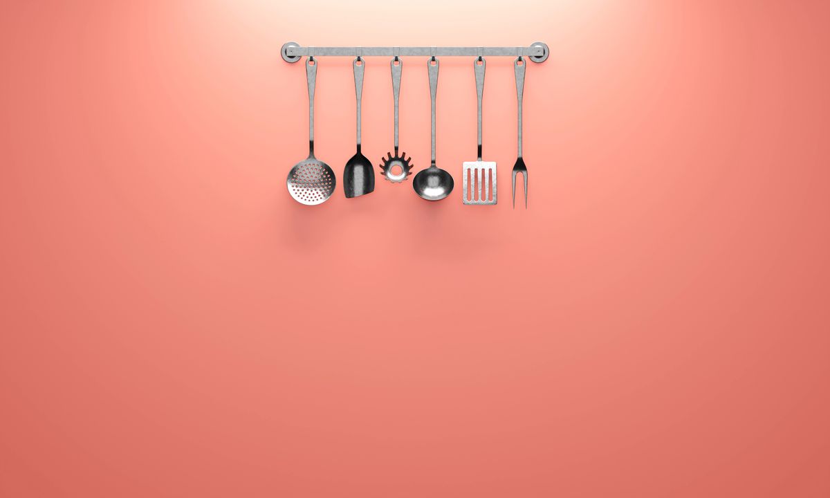 Hanging kitchen utensils against a coral backdrop, ideal for minimalistic design concepts.