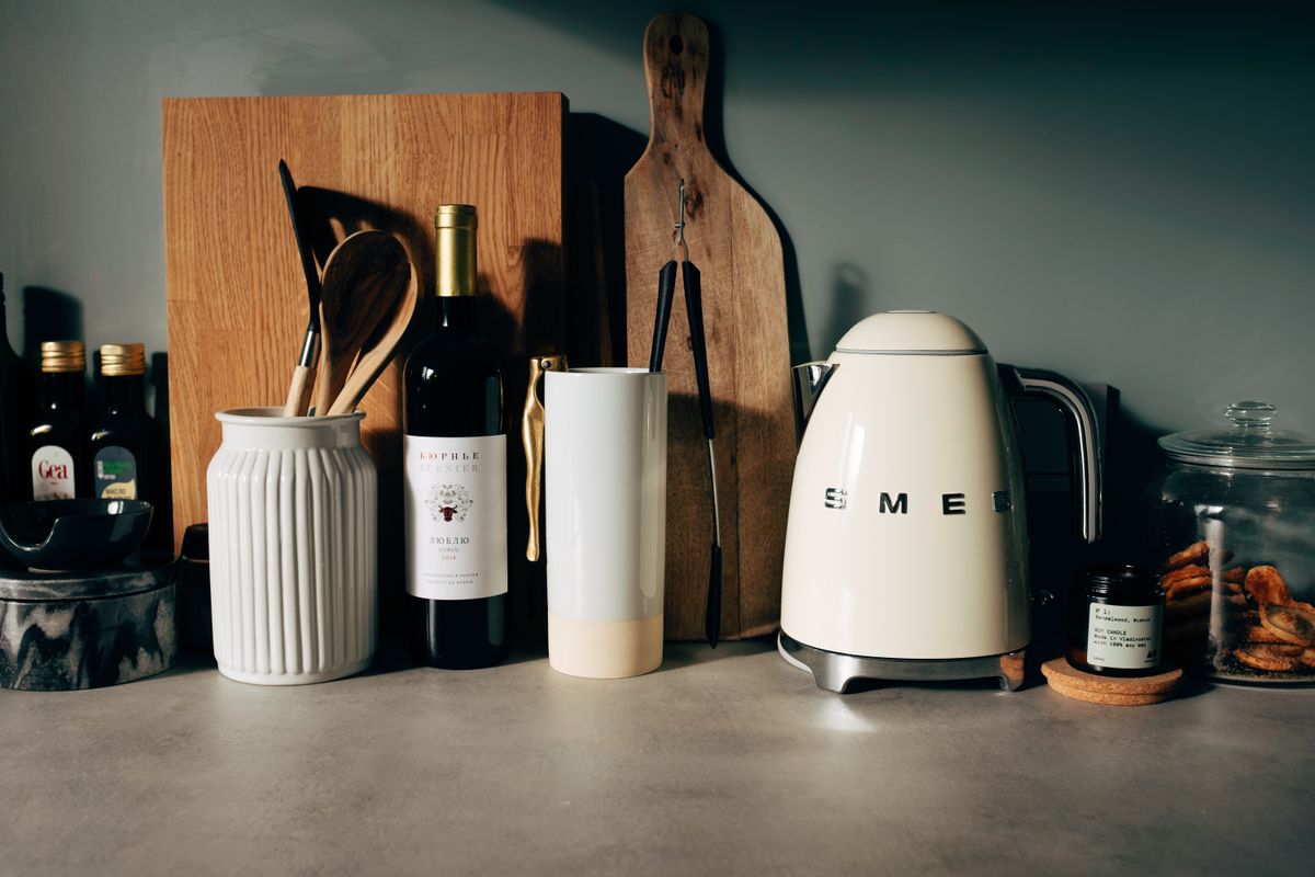 White gloss electric kettle standing next to other kitchen utensils with bottle of wine and various bowls on countertop in modern home kitchen