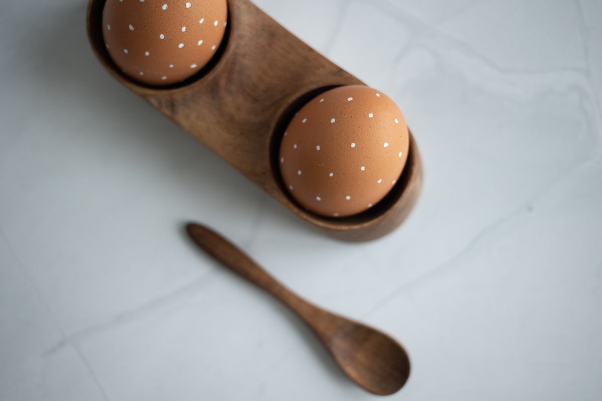 Artistic eggs with polka dots in a wooden holder and spoon setup.