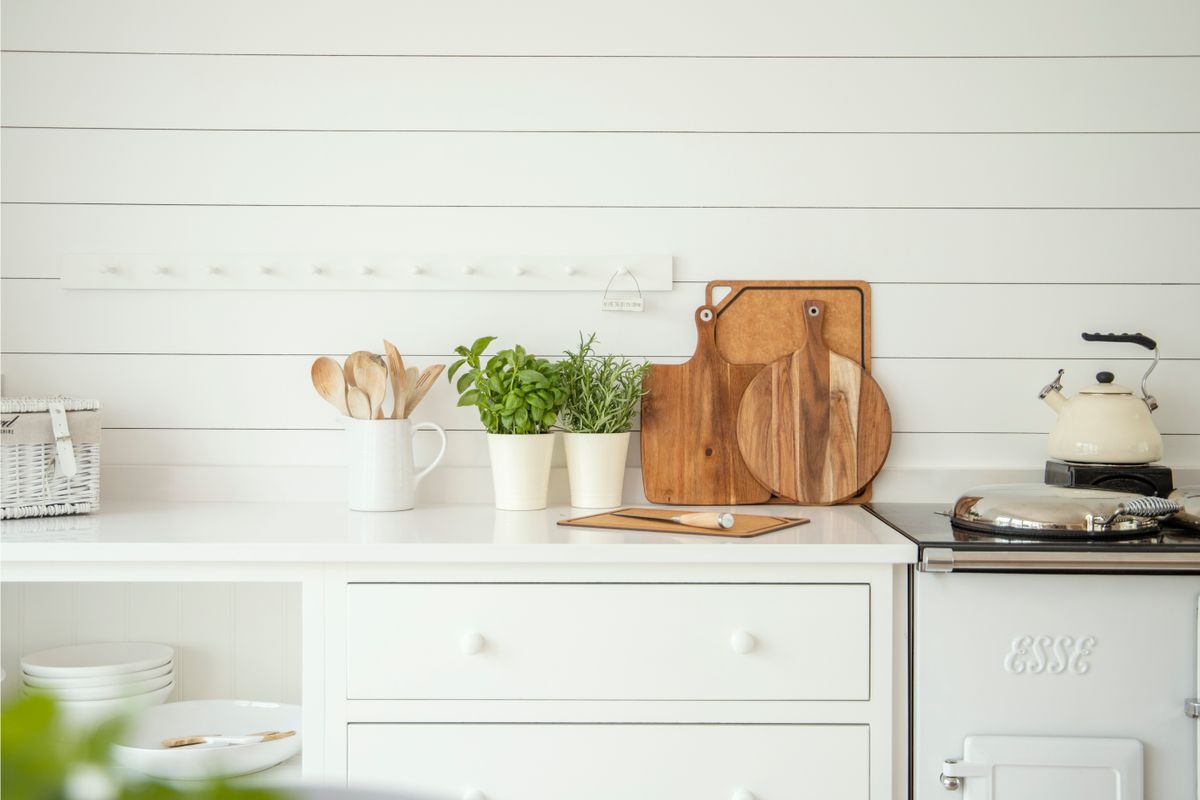 Stylish kitchen counter with herb pots, cutting boards, and utensils against a white backdrop.