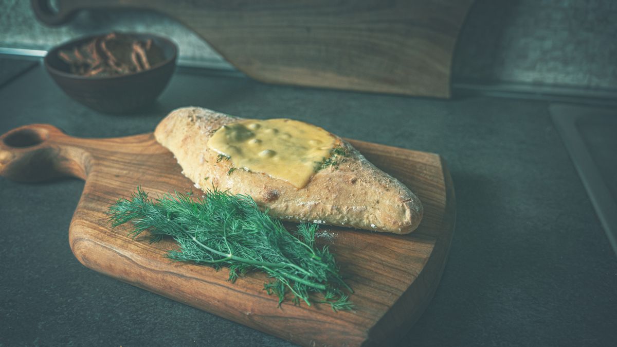 Fresh bread with melted cheese and dill on a wooden board in kitchen setting.